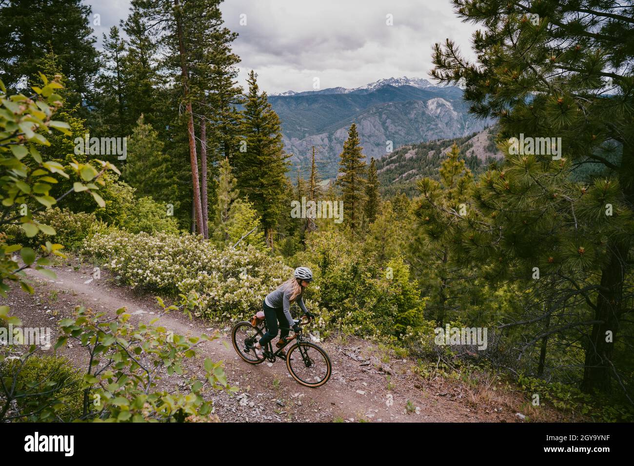 Woman bikes on rocky ridge trail overlooking mountain valley Stock Photo