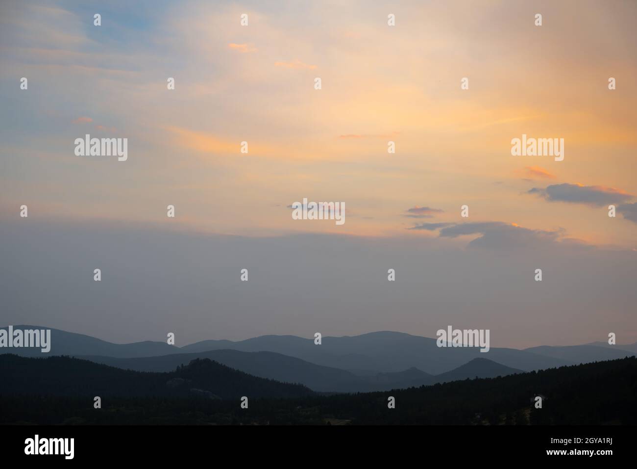 Smoke causes mountains to be layered with an orange sunset above them Stock Photo