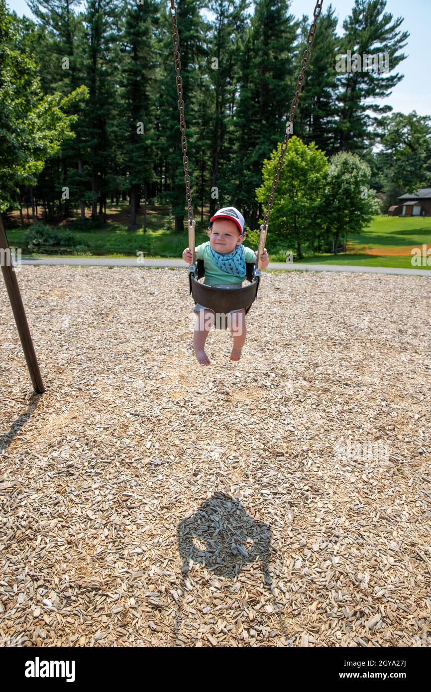 Adorable baby boy wearing baseball cap swinging alone at the park. Stock Photo