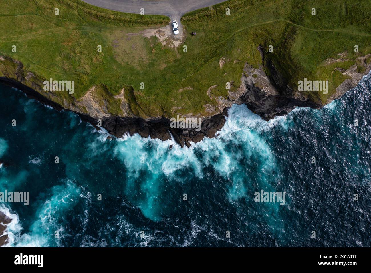 Birds eye view of car parked at end street of the famous Moher Cliff in Ireland with waves hitting the rocks during day. Stock Photo