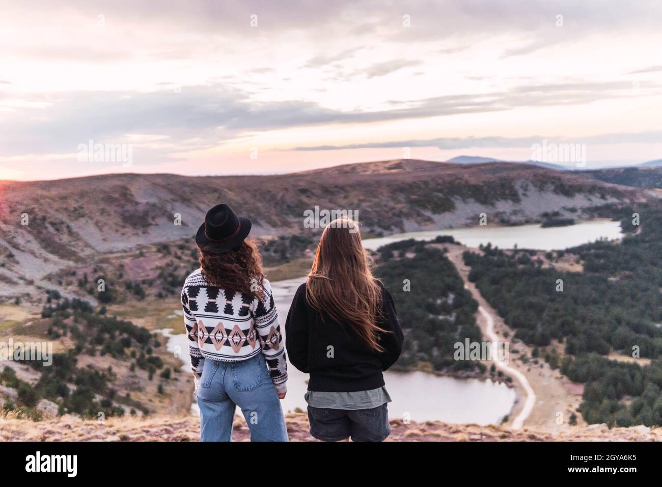 rear view of two women standing next to a lake with mountains Stock ...