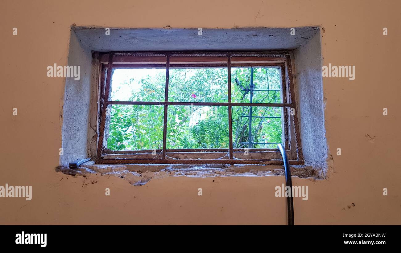 A rectangular basement window is tightened with a metal mesh and a grill. Technical window in the wall of an old gray building Stock Photo