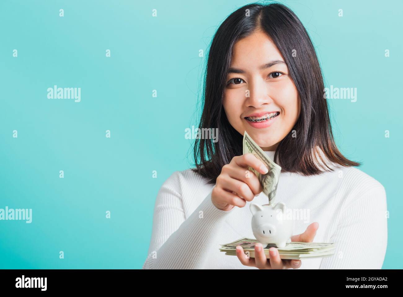 Asian beautiful young woman holding piggy bank on hands and putting ...