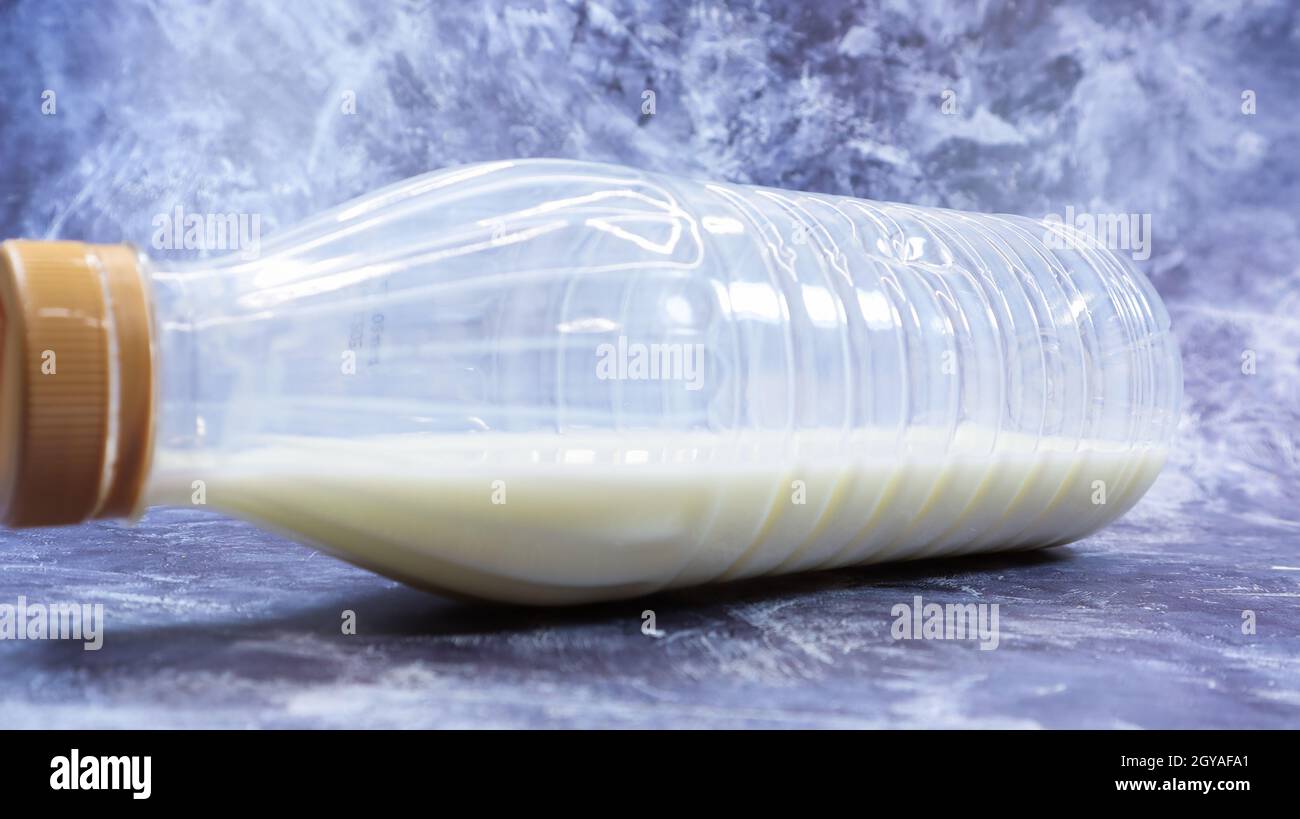 A semi-empty plastic bottle of fresh regular milk lies on a dark gray marble or concrete backdrop. Close-up front view. World milk day concept. Nutrie Stock Photo