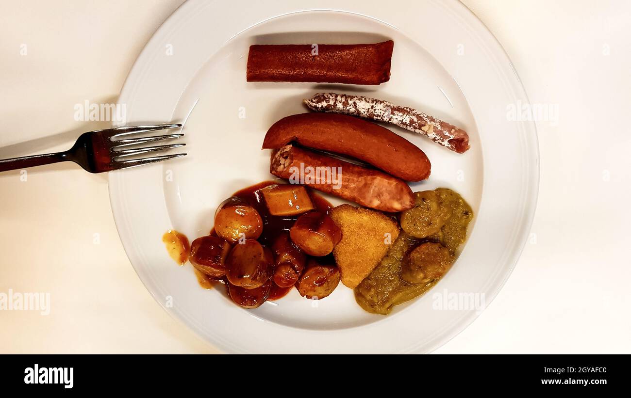 Assorted German sausages on a white plate with a fork in a pub. Traditional German food in a plate. Carrivurst, Bratwurst, Thuringian, Weisswurst, Nur Stock Photo