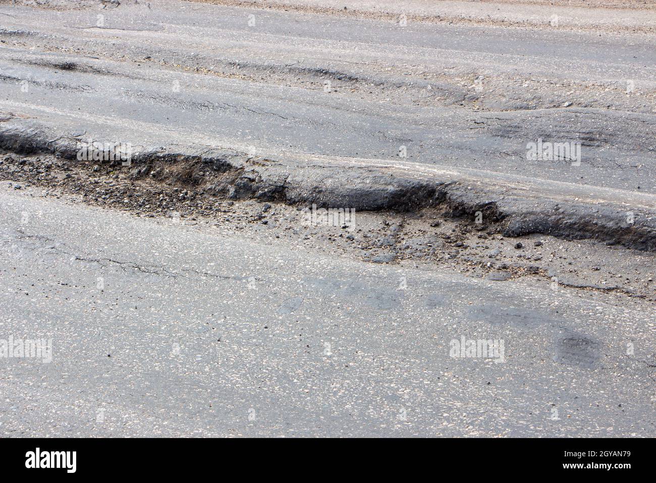 Poor condition of the road surface. Spring season. Hole in the asphalt, risk of movement by car, bad asphalt, dangerous road, potholes in asphalt. Moa Stock Photo
