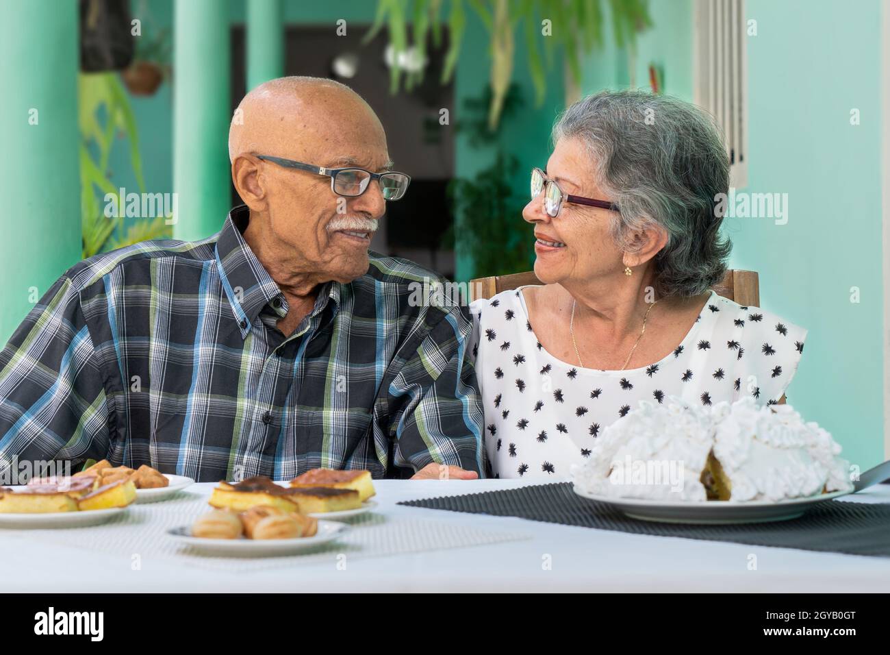 Elderly couple wearing glasses sitting at a table, both are smiling Stock Photo
