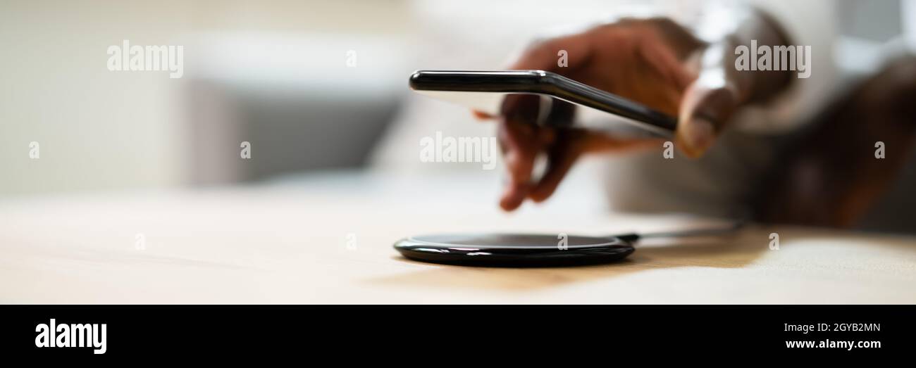 Man Charging Smartphone Using Wireless Charging Pad At Home Stock Photo