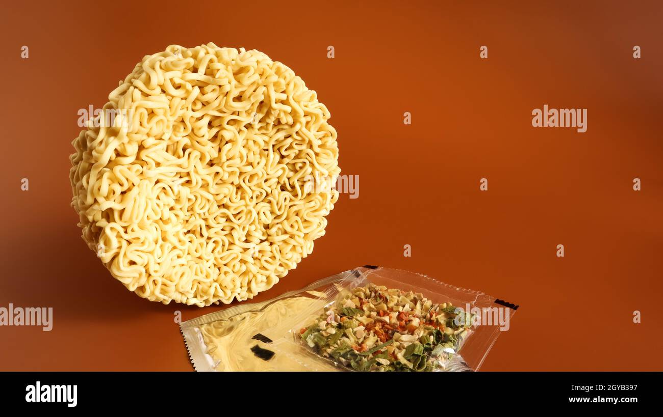 circle of instant noodles with raw spices on a plain brown background