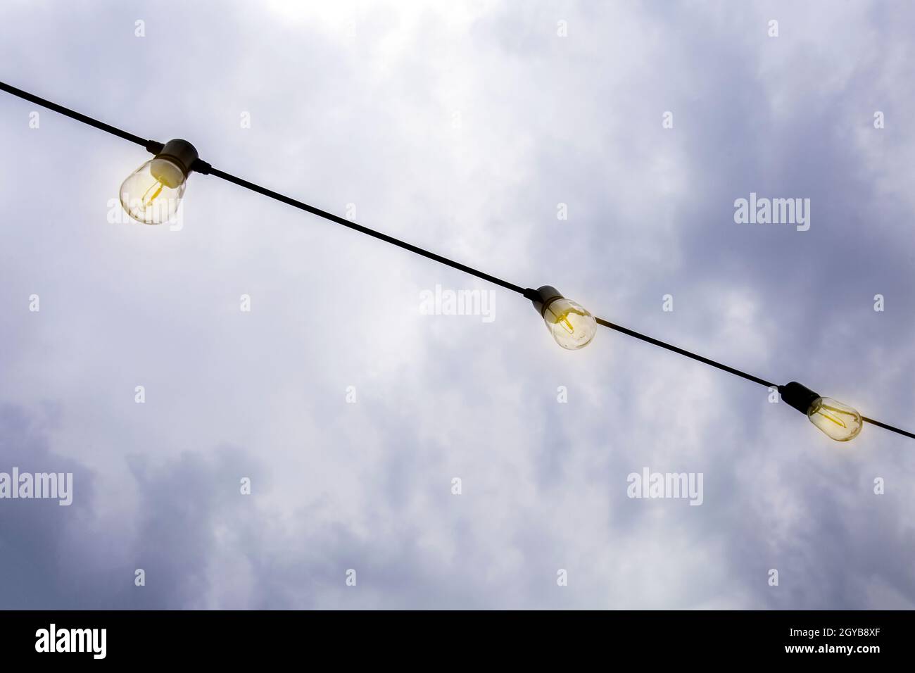 Glowing Light bulbs hanging against the dark evening sky, in a row modern decoration with copy space moody Stock Photo