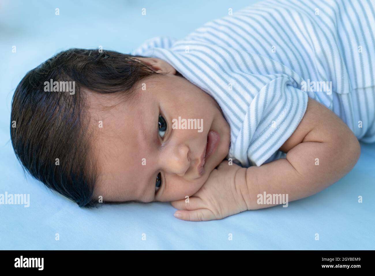Infant lying on his stomach with his eyes open on a blue diaper Stock