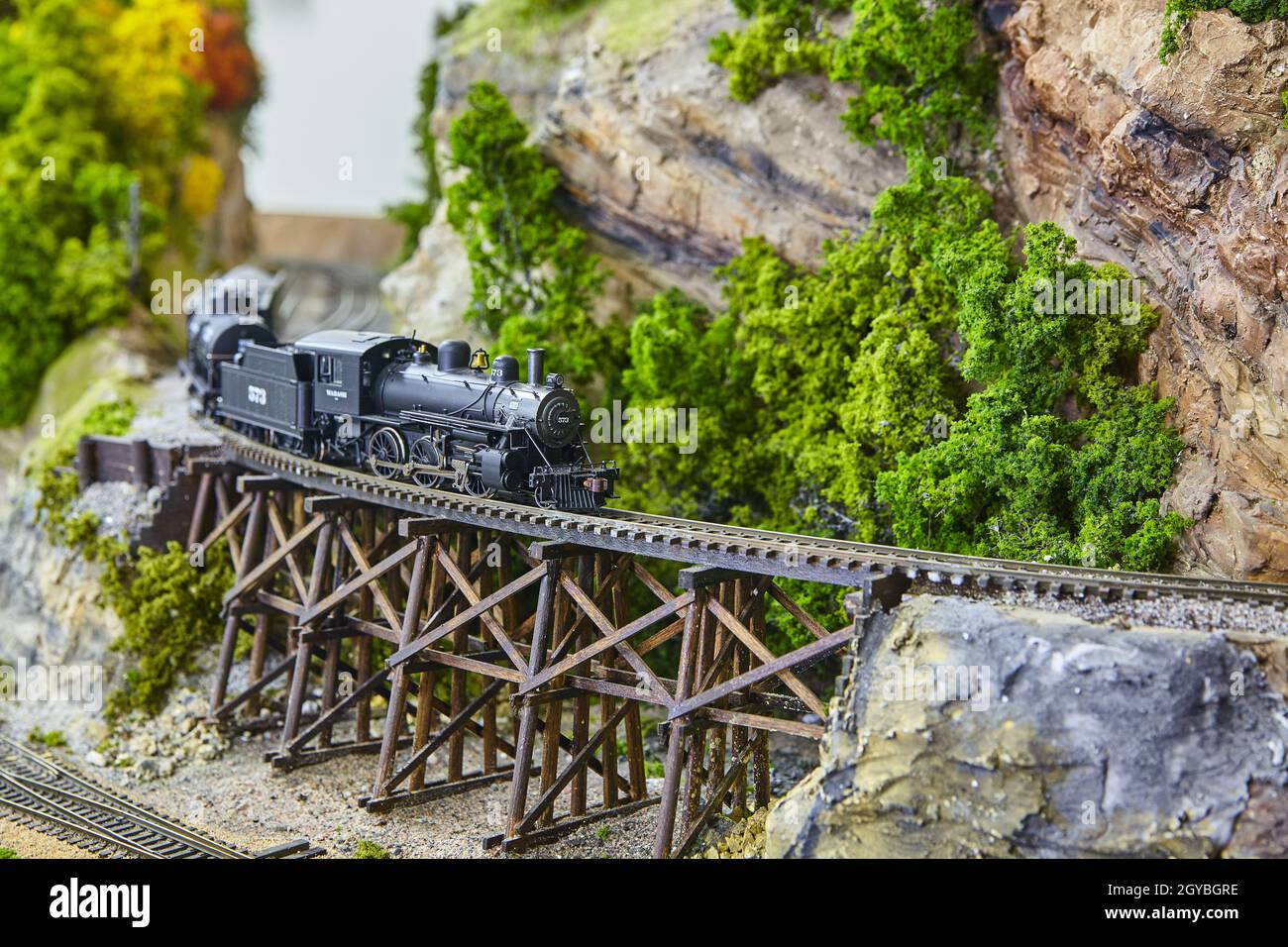 A miniature toy train on railroad track next to mountain with moss as