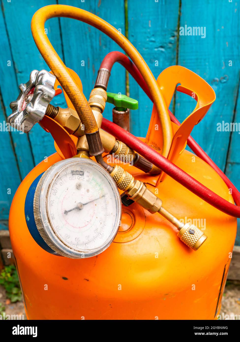 Refrigerant cylinder and hoses with pressure gauge. Orange bottle with