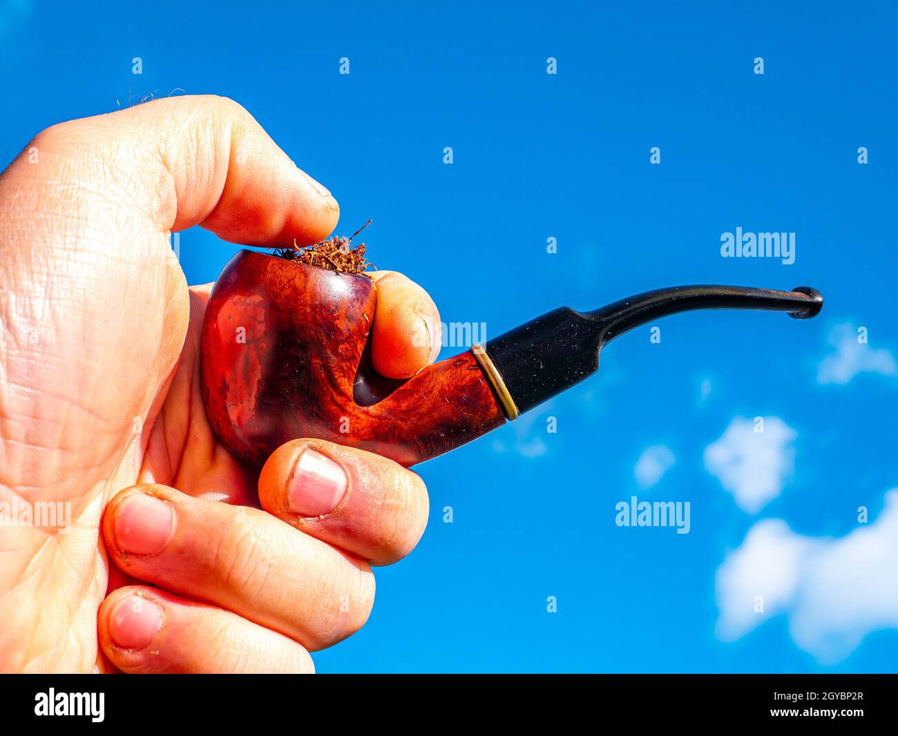 Wooden smoking pipe for tobacco in hand against blue sky background