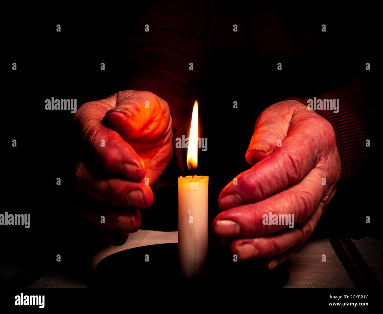 The flame of a burning wax candle in the hands of an old man. The flame