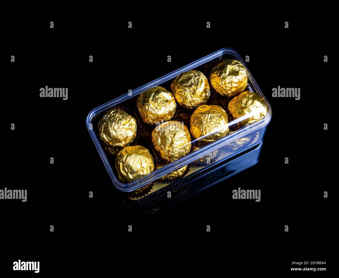 A box of round chocolates in a golden wrapper on a black background