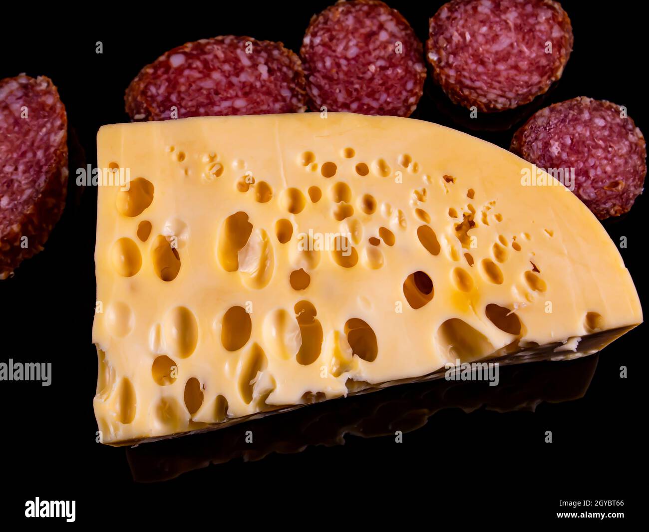 A piece of hard cheese and a sliced sausage on a black background. Hard cheeses. Meat sausage. Milk product. Meat sausages. Dairy products. Home kitch Stock Photo