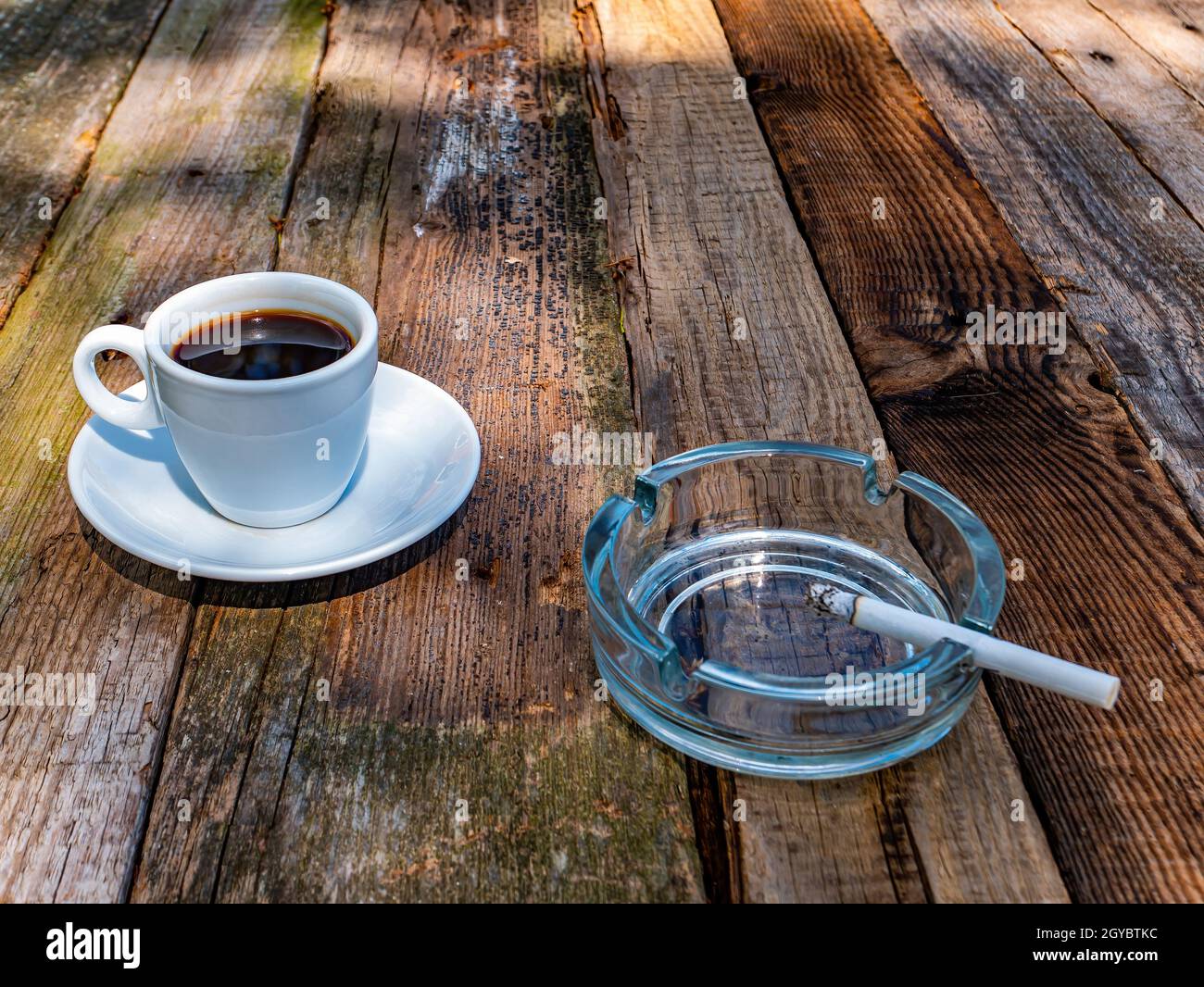 espresso cup with cigarette holder A cup of coffee and a glass ashtray with a cigarette on a wooden table.  Coffee drink. A cigarette in an ashtray. Wooden table. Hot drink. Street  Cafe Stock Photo