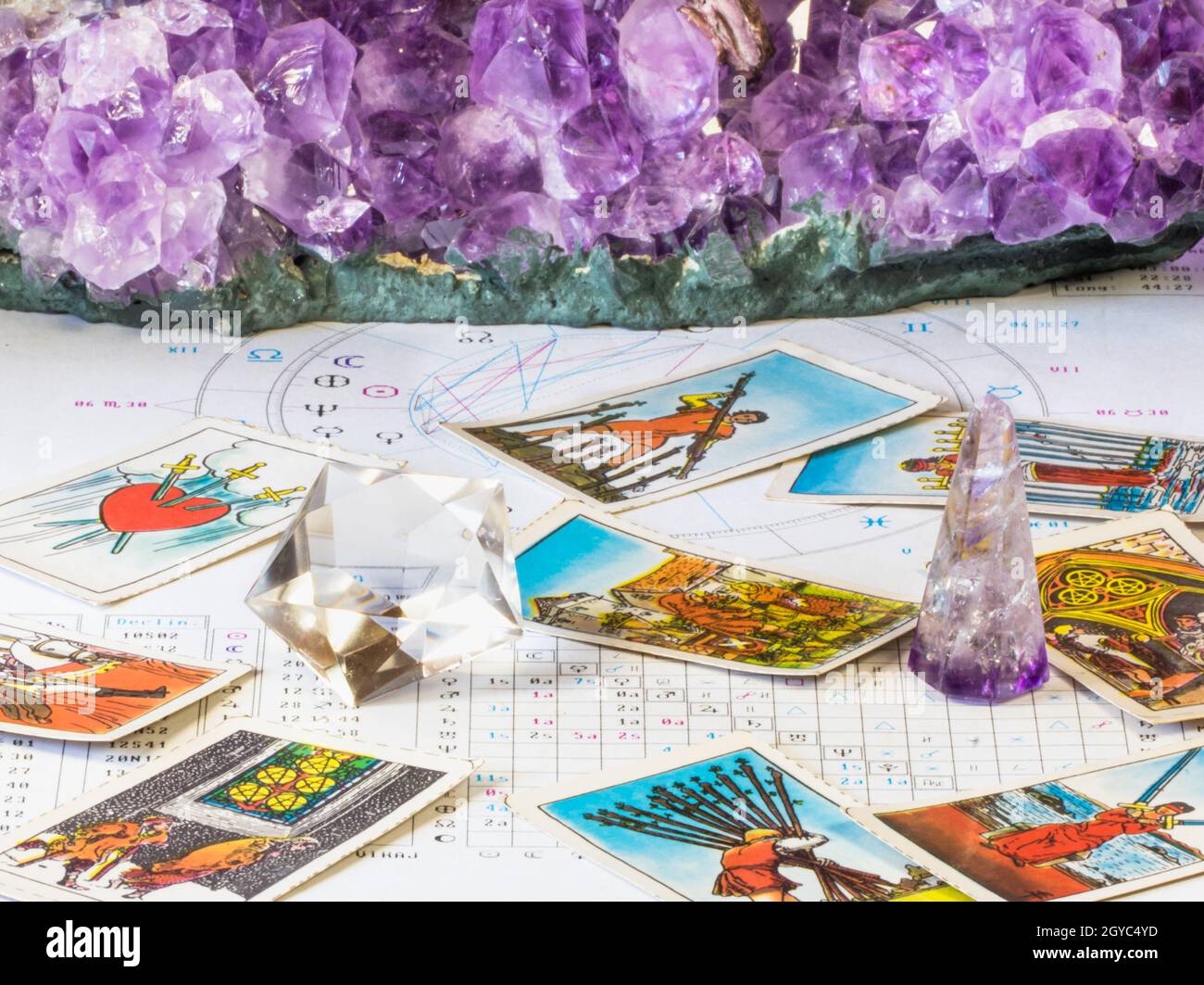 Closeup shot of tarot cards and amethyst crystals over a white birth chart in astrology style
