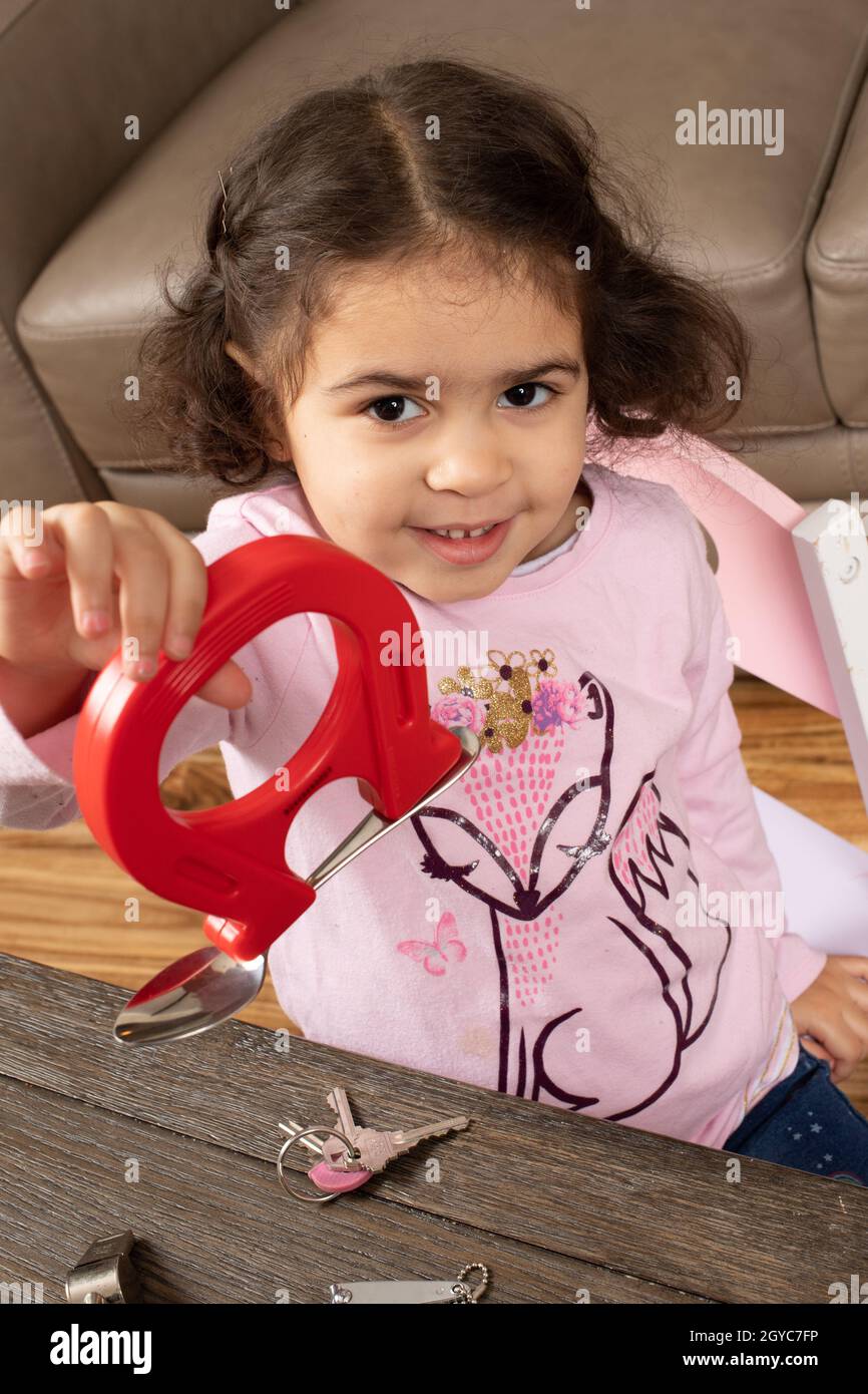 Three year old girl playing with magnet and metal objects, proudly holding up magnet with metal object attached Stock Photo