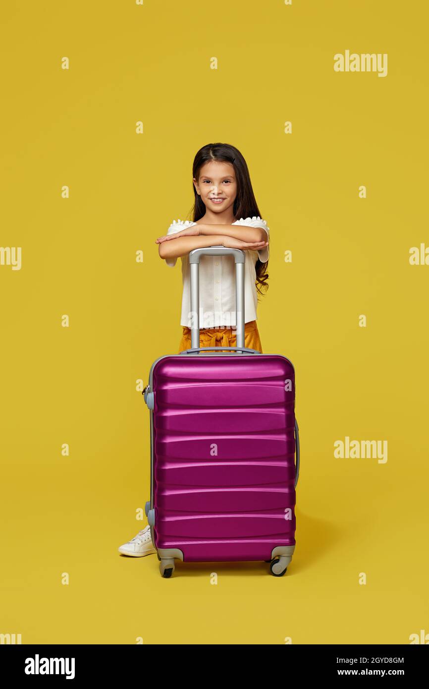 Happy little child girl with pink suitcase going traveling on yellow