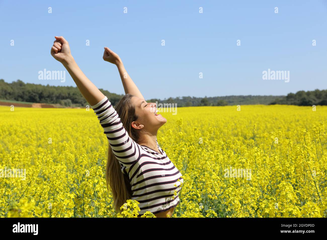 Excited woman raising arms in a yellow field celebrating spring a sunny ...