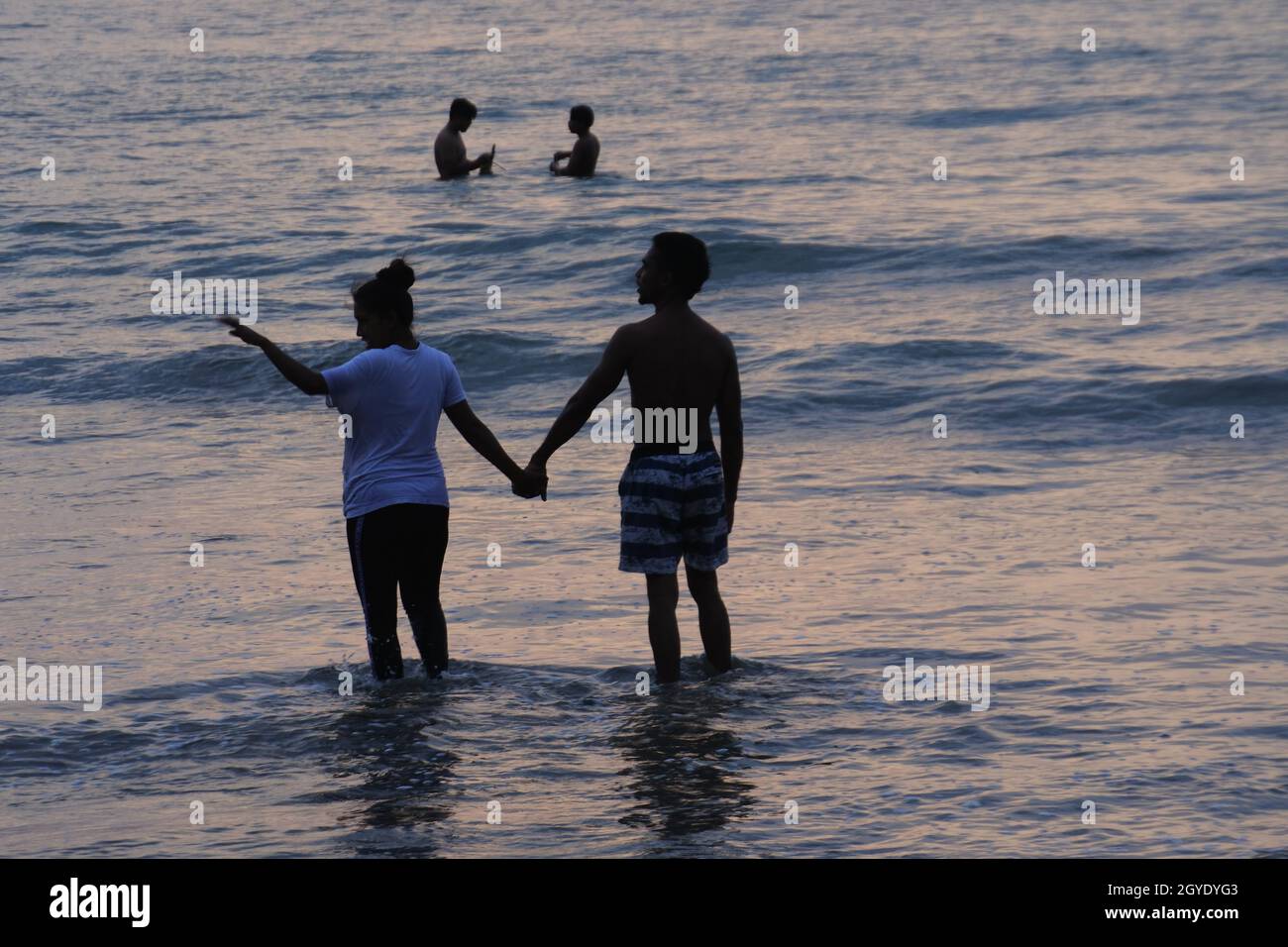 Horizontal shot of a couple entering the sea and people swimming in the distance Stock Photo