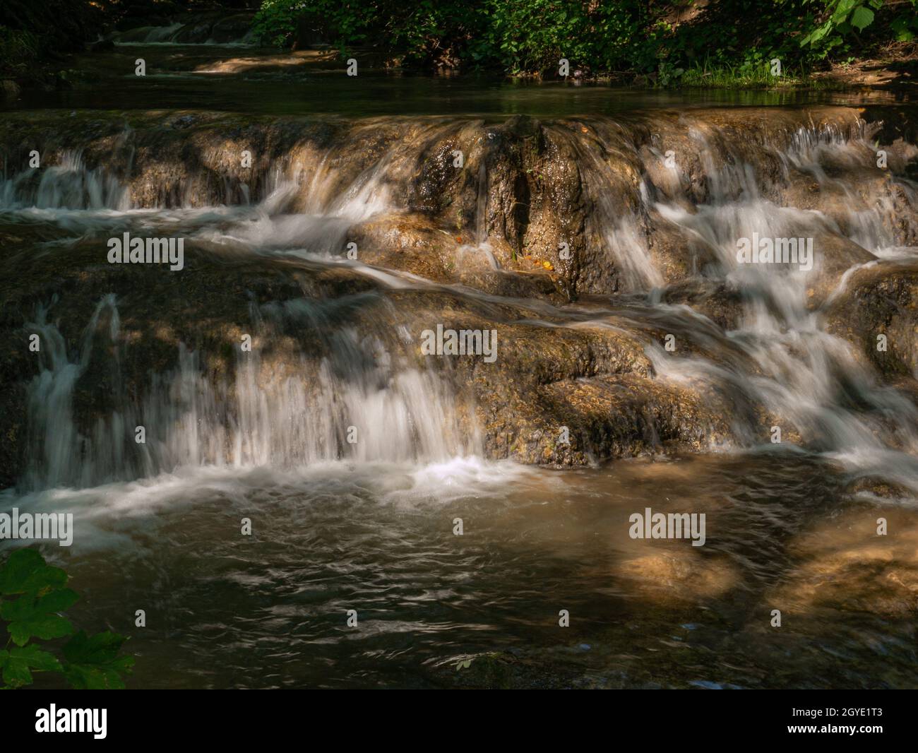 Das klare Wasser fließt über den braunen Felsen im Bach Stock Photo