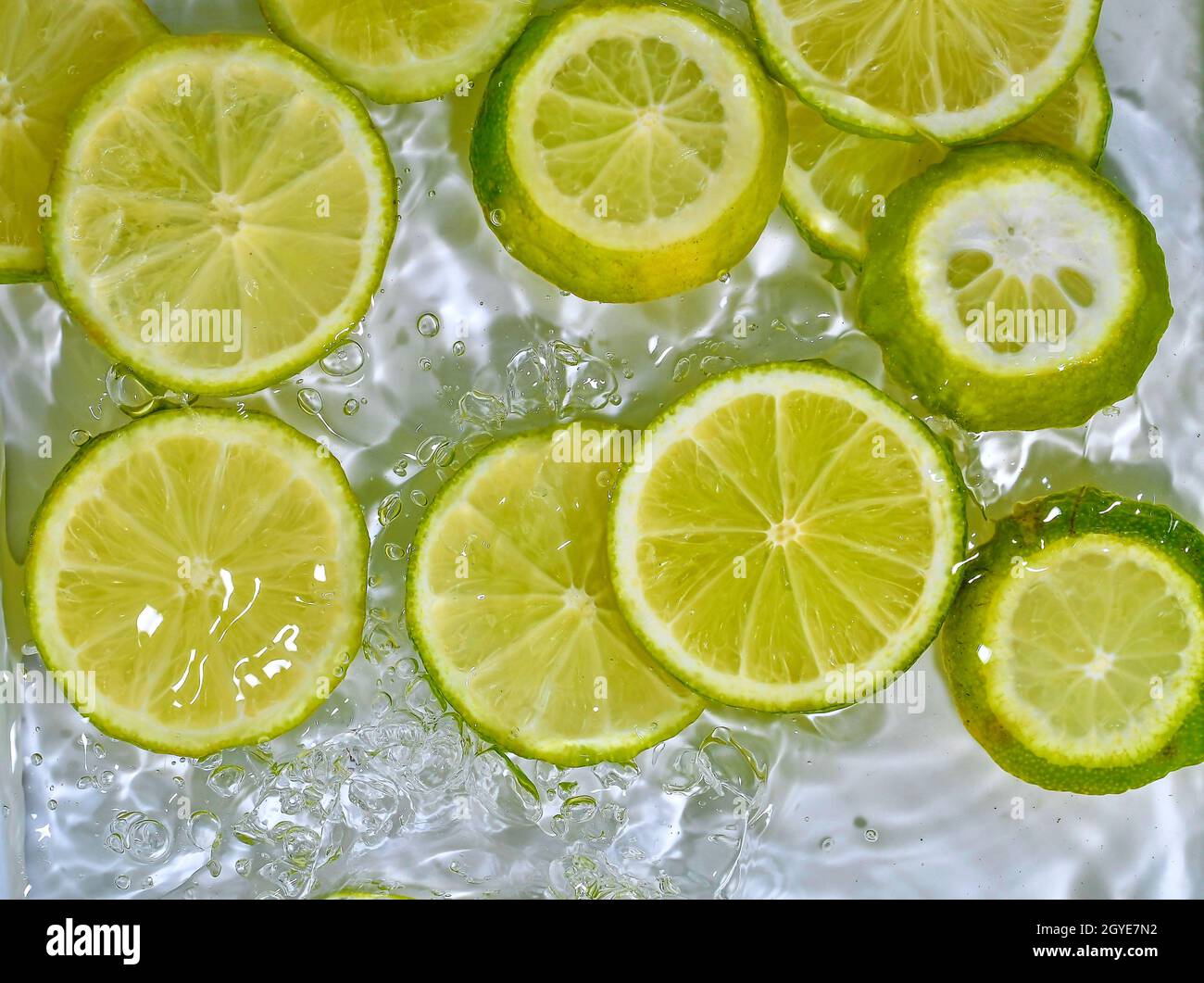 Close-up fresh slices of green limes on white background. Slices of limes in sparkling water on white background, closeup. Citrus soda. Copy space. Stock Photo