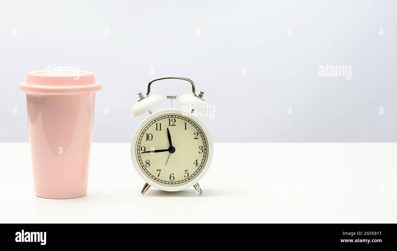 round retro alarm clock and pink ceramic cup with coffee on white table Stock Photo