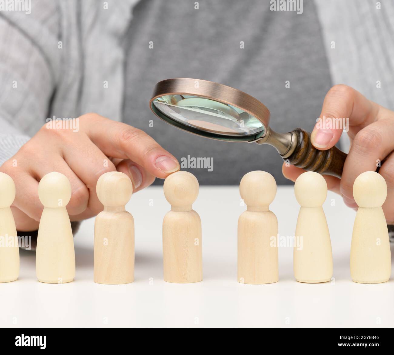 figurines of men on a white table, a female hand holds a magnifying glass over one. concept of searching for employees in the company, recruiting pers Stock Photo