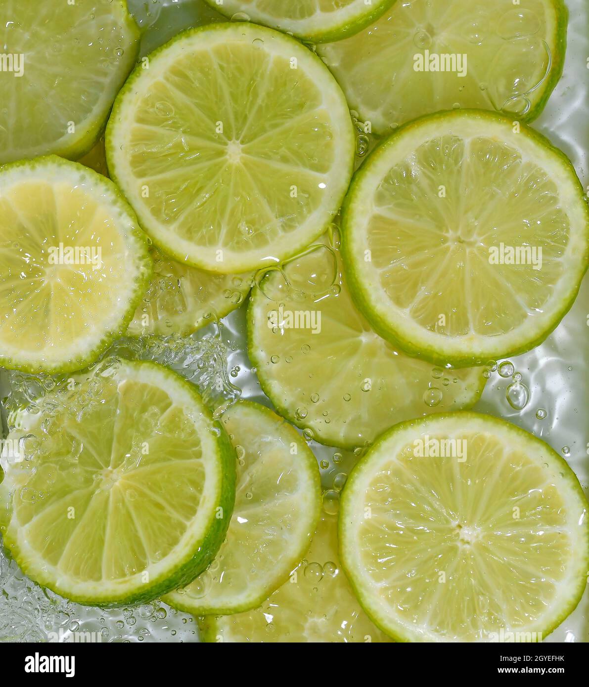 Close-up fresh slices of limes on white background. Slices of limes in sparkling water on white background, closeup. Citrus soda. Stock Photo