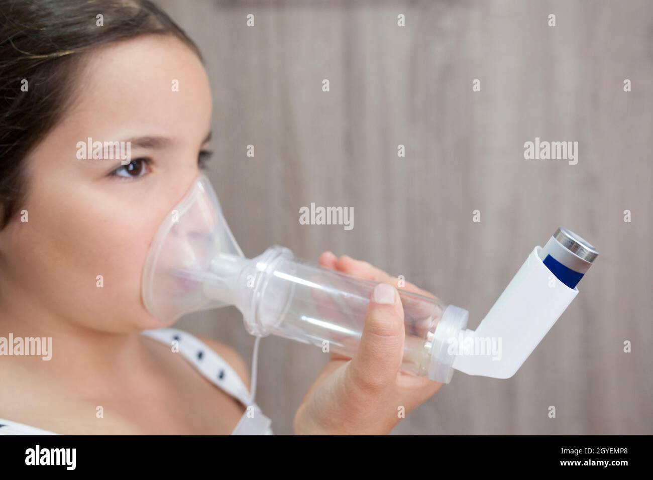 Child girl using medical spray for breath. Inhaler, spacer and mask. Side view Stock Photo