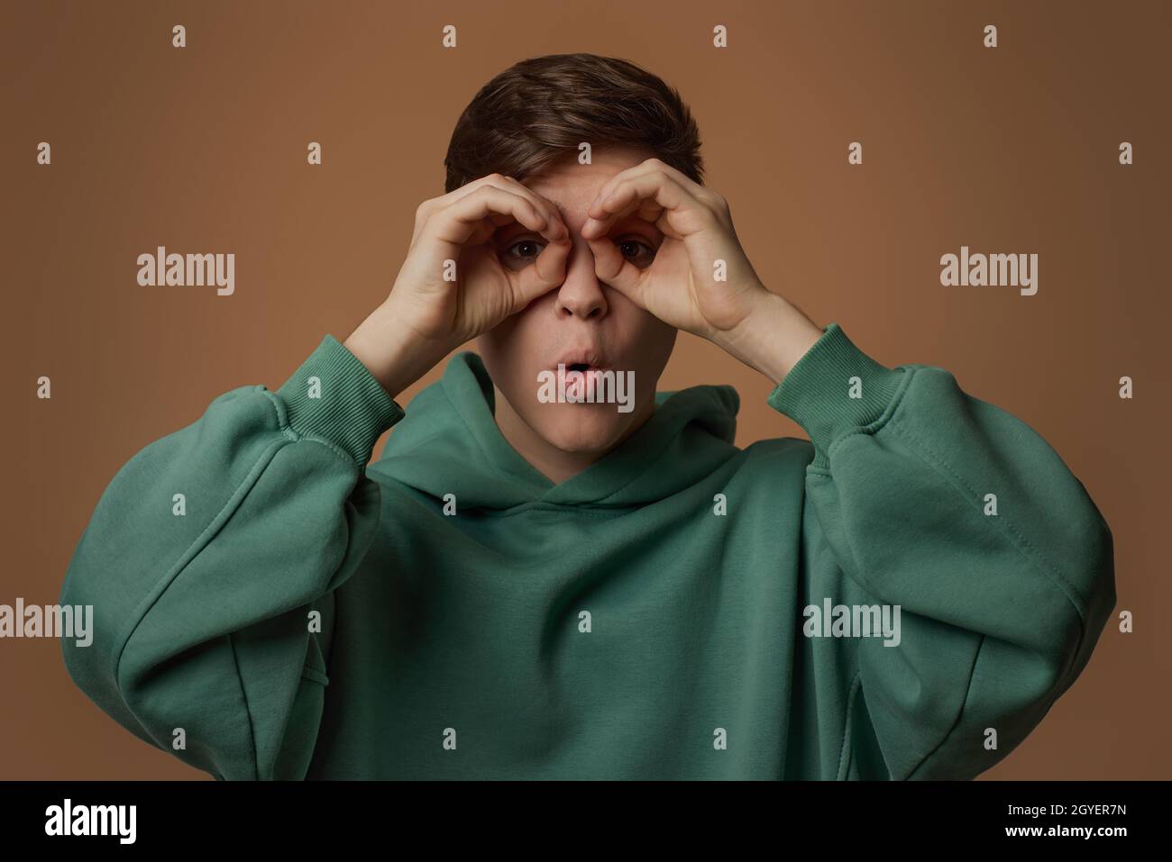 young guy in sweatshirt holding his hands at his eyes as if looking through binoculars Stock Photo