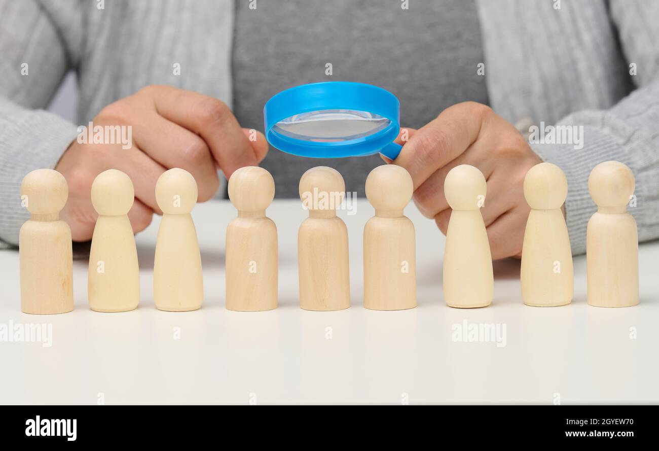 figurines of men on a white table, a female hand holds a magnifying glass over one. concept of searching for employees in the company, recruiting pers Stock Photo