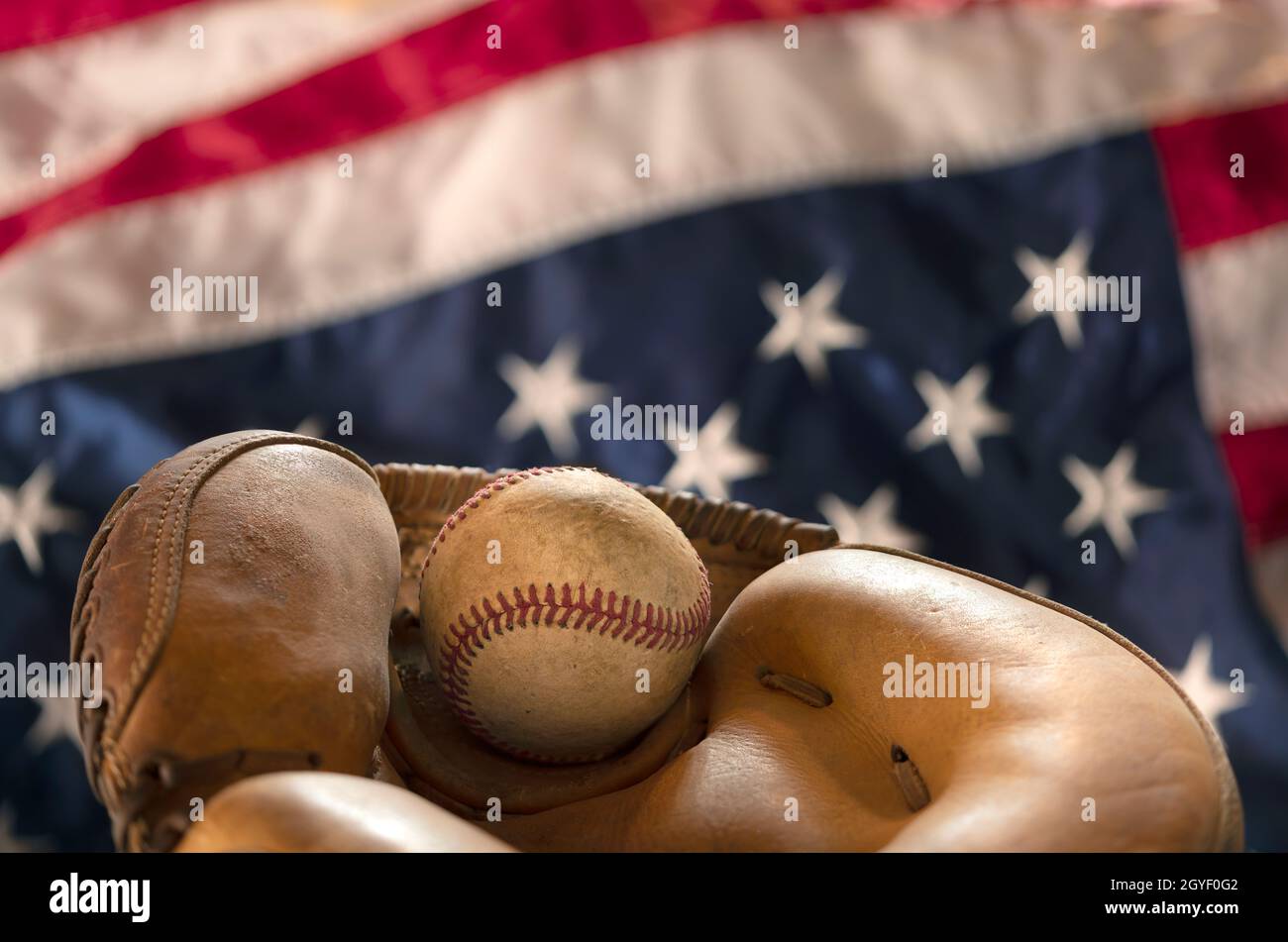 Close up of an old baseball and glove against the American flag highlights one of the most popular sports in the country. Stock Photo