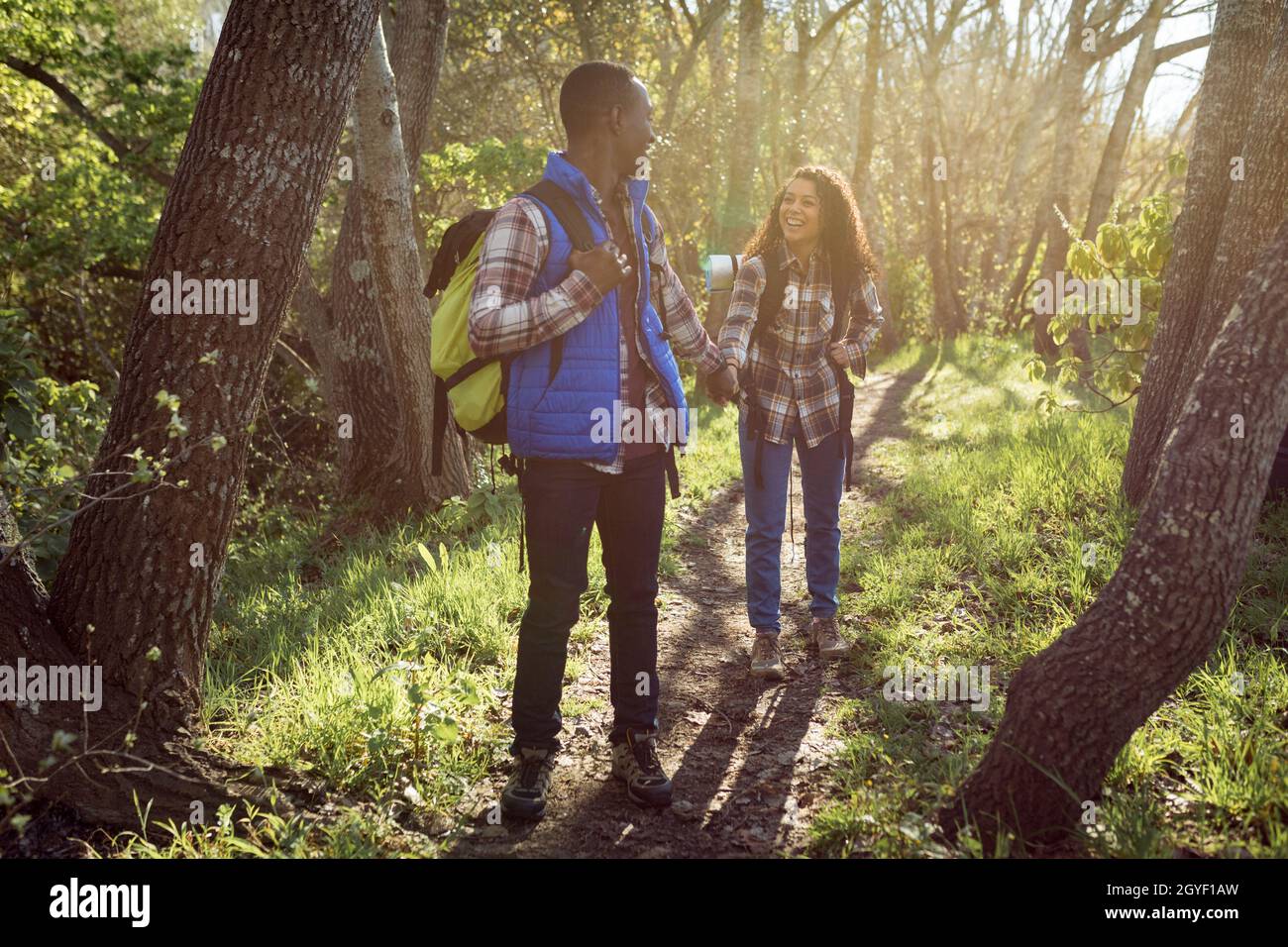 Happy diverse couple with backpacks hiking in countryside Stock Photo