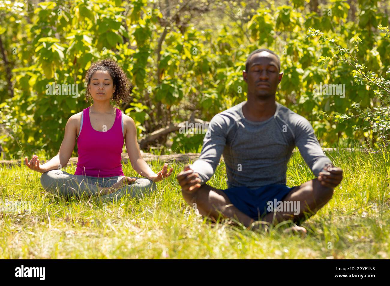 Relaxing diverse couple sitting with crossed legs and meditating in countryside Stock Photo