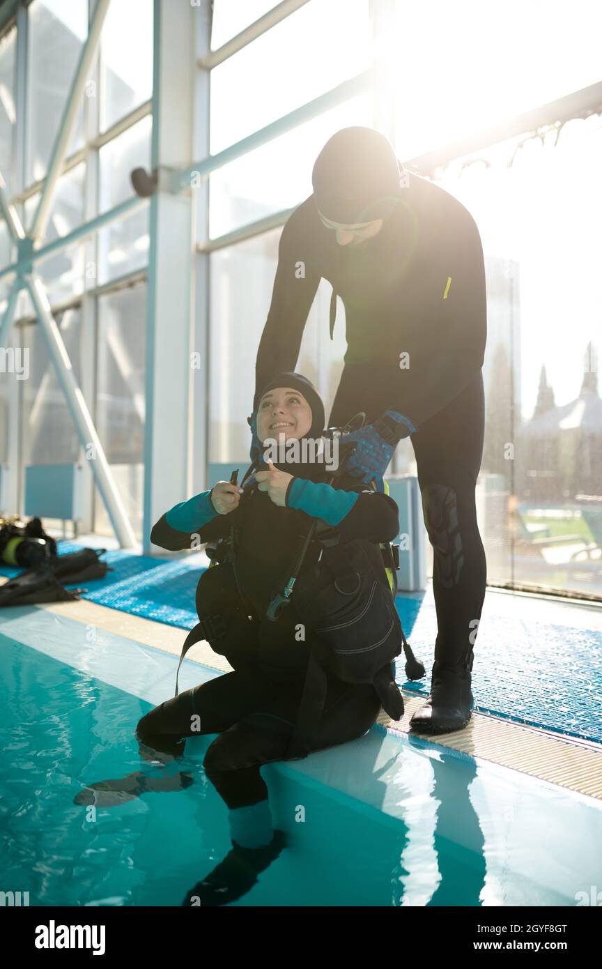 Male instructor helps woman to set up scuba gear, diving school ...
