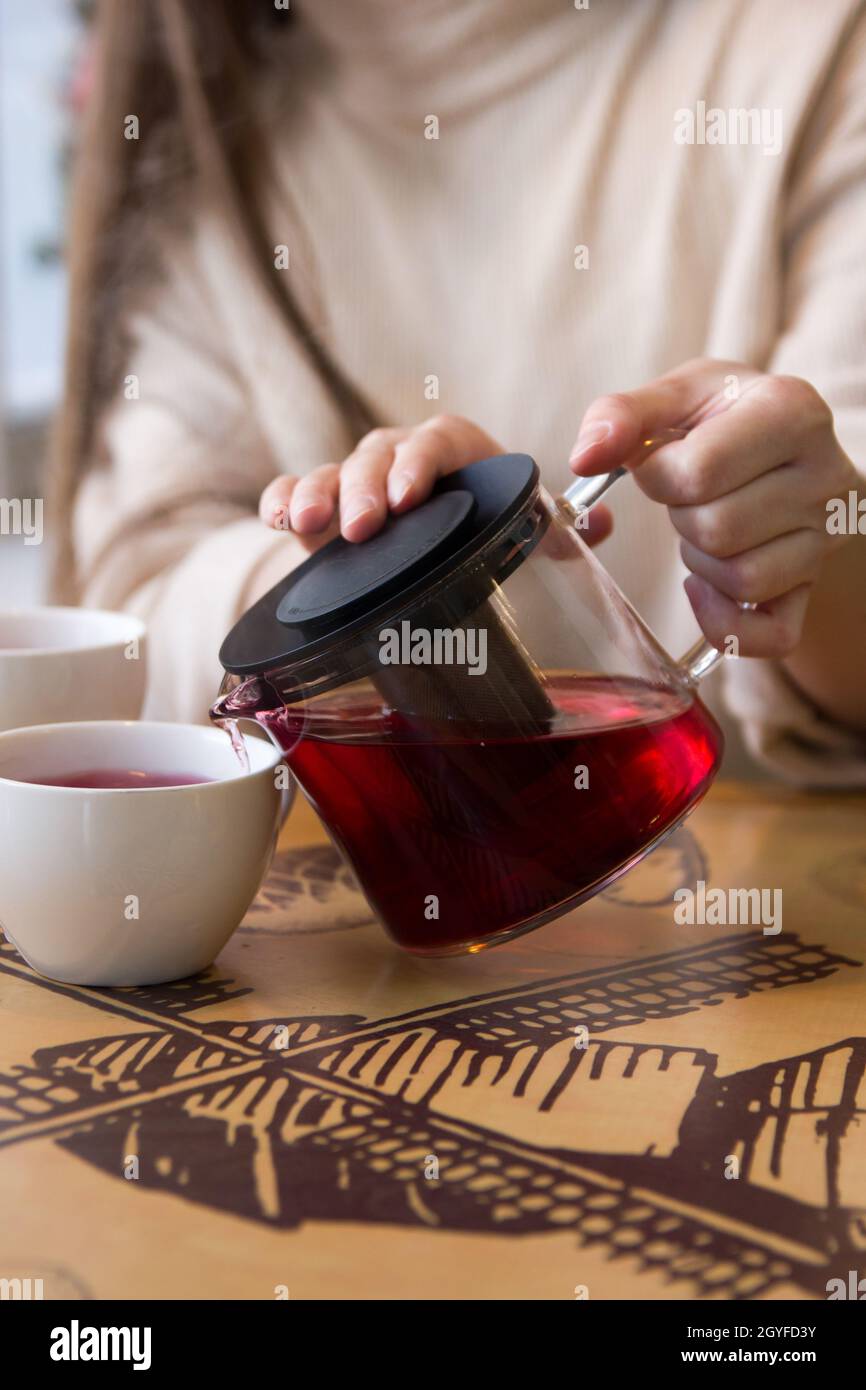 Pour the hot tea into a cup. The cup of tea on the wooden table was illuminated by the soft sunlight that penetrated the warm atmosphere Stock Photo