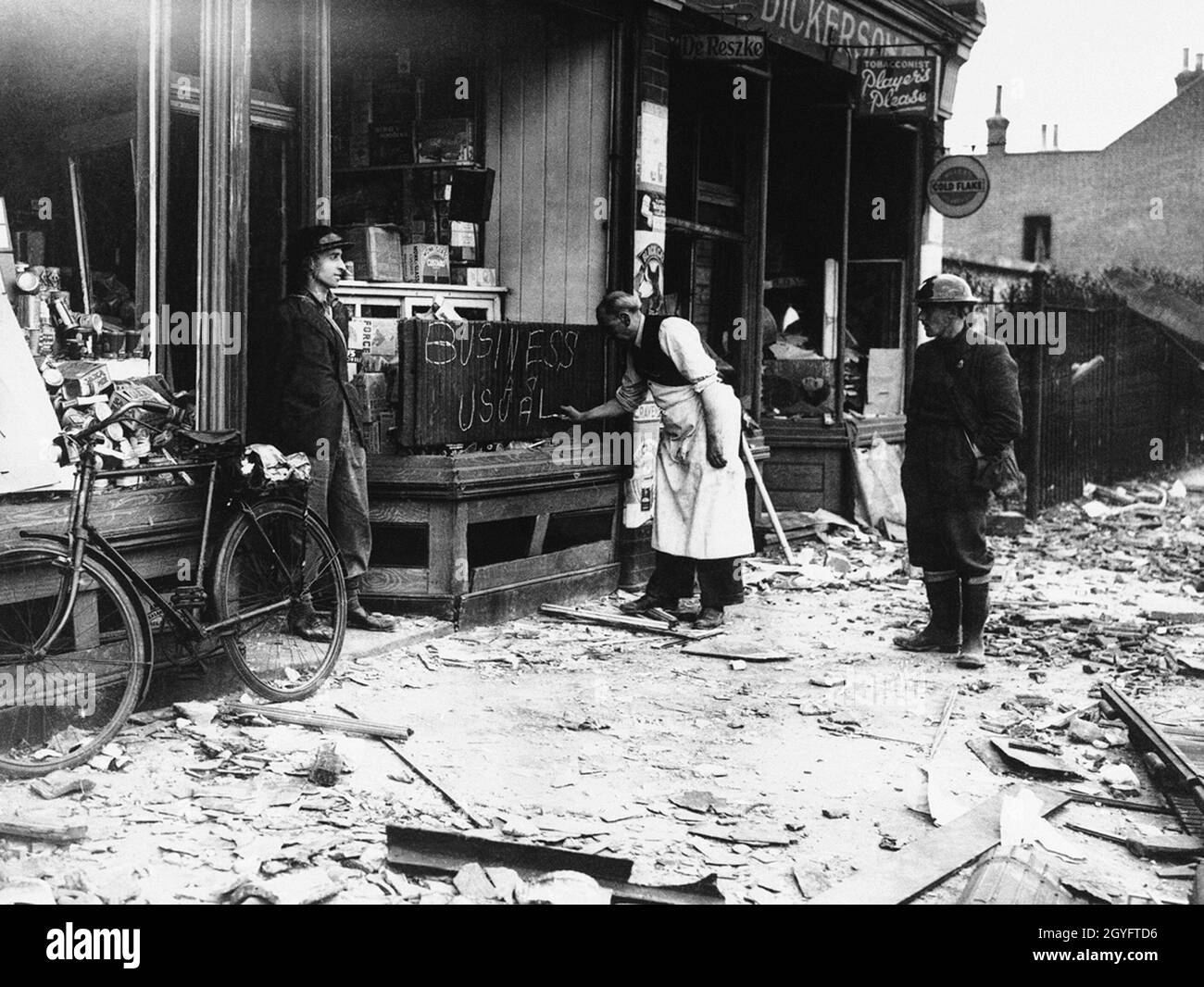 A shopkeeper writing Business As Usual on a blackboard outside his damaged shop in London during the Blitz, England 1940 Stock Photo