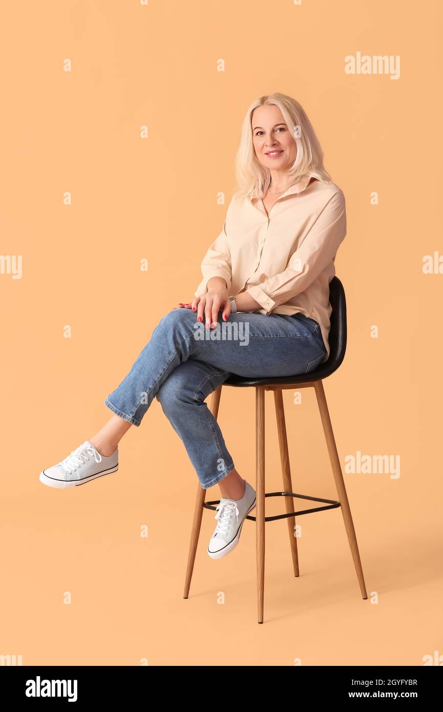 Beautiful mature woman sitting in chair on beige background Stock Photo ...