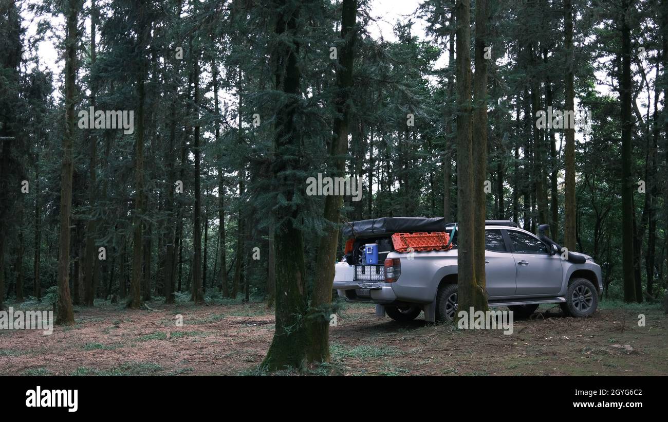 Pickup car with tent on the roof and alone man cooking in the forest. Adventure travel lifestyle