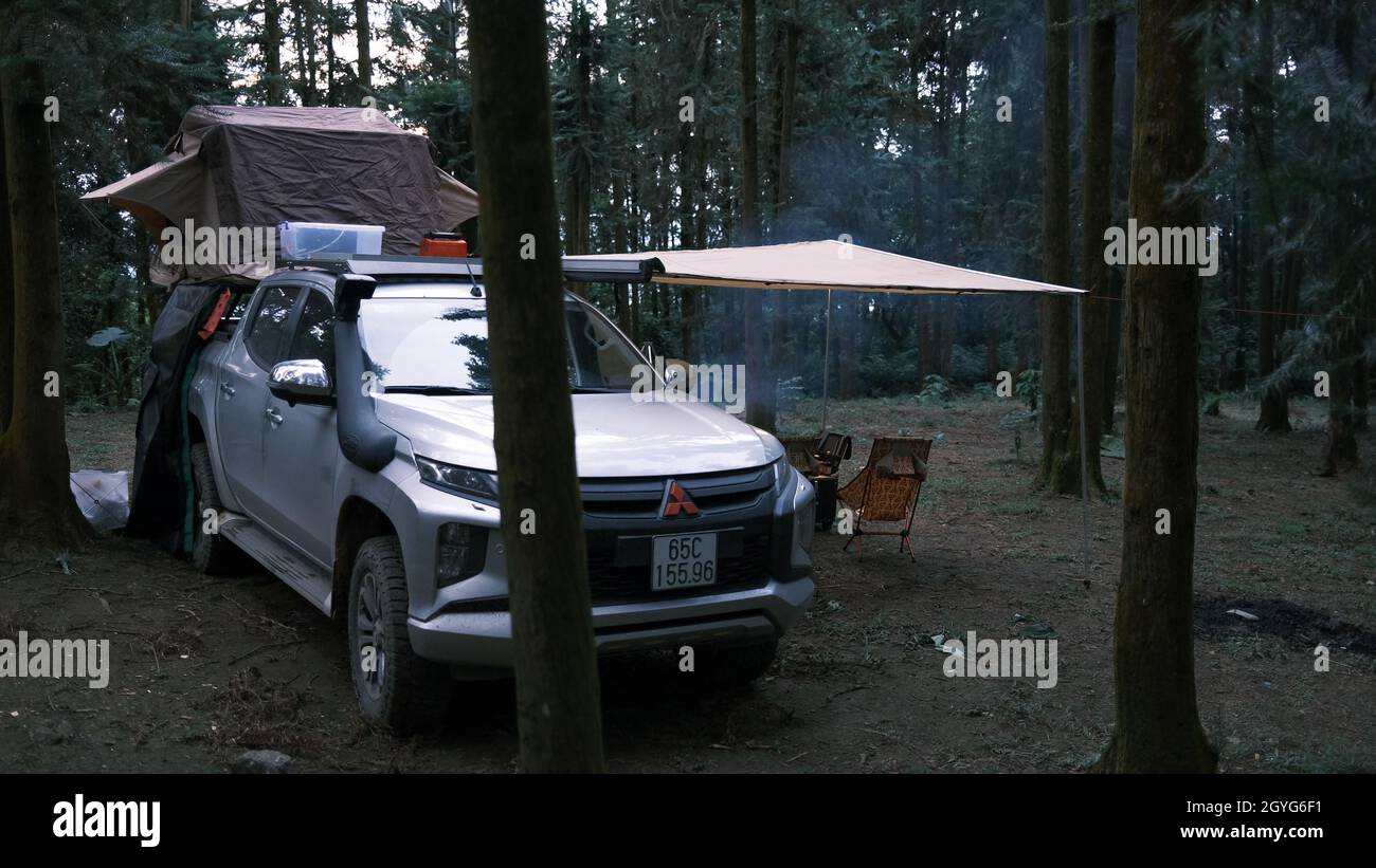 Pickup car with tent on the roof and alone man cooking in the forest. Adventure travel lifestyle