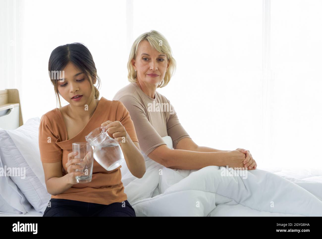 Asian daughter pour water into a glass for her adopted caucasian mother. Concept of love and sharing time of family, mother or daughter in law. Stock Photo