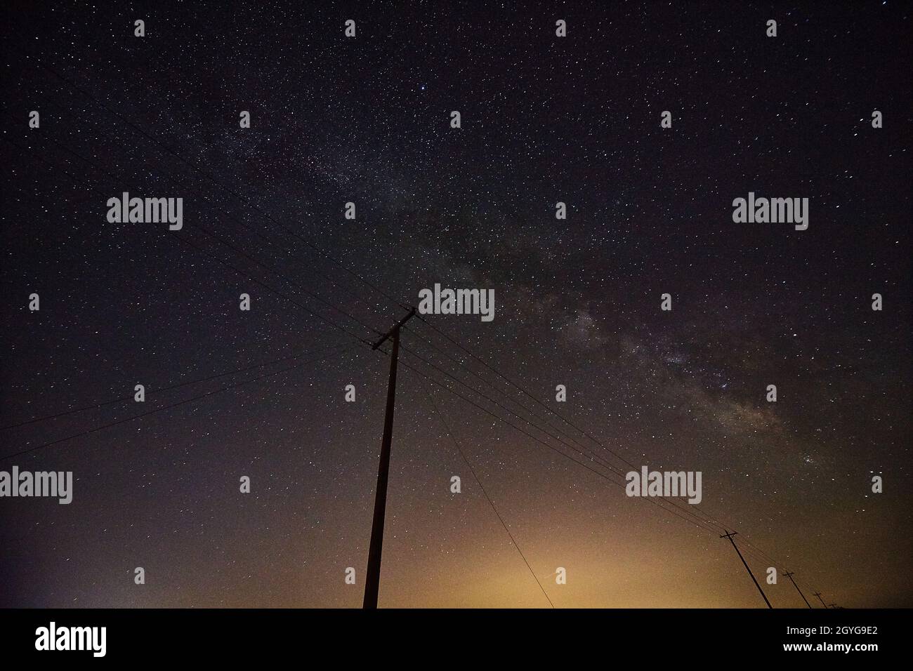 City glow with a stary night sky and the silhouette of telephone poles Stock Photo
