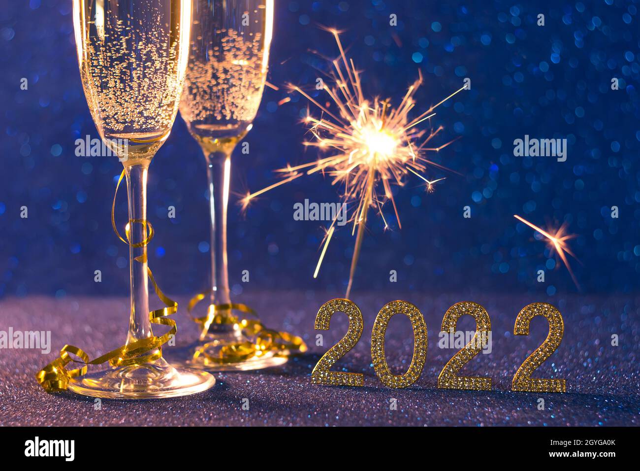 Happy new year 2022 .Christmas and New Year holiday background with two cups, a glass of champagne and sparklers on a blue background with bokeh Stock Photo