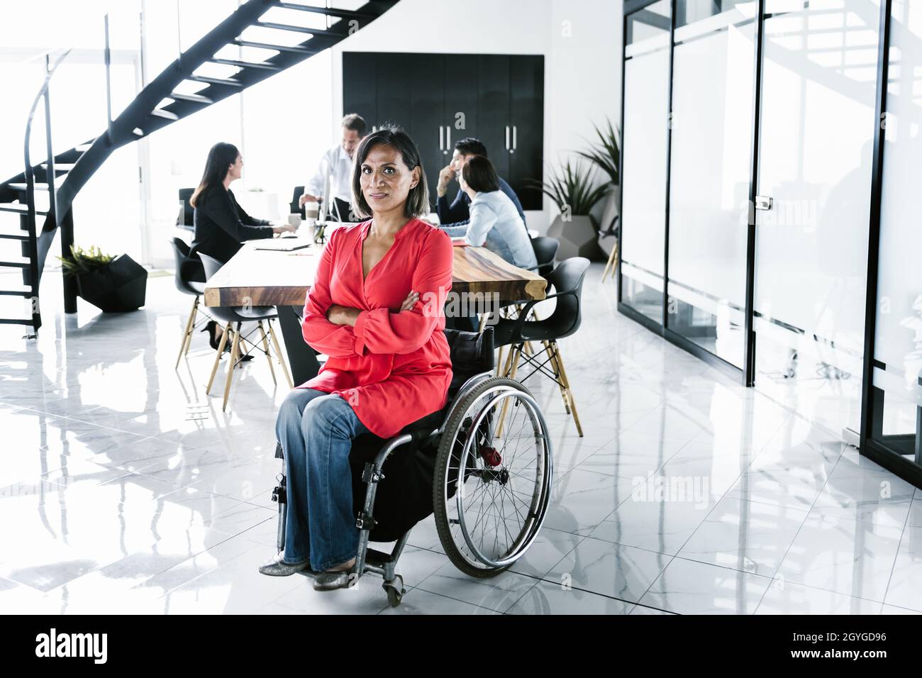 Portrait of latin transgender woman in wheelchair and people at meeting in the background in the office in Latin America Stock Photo