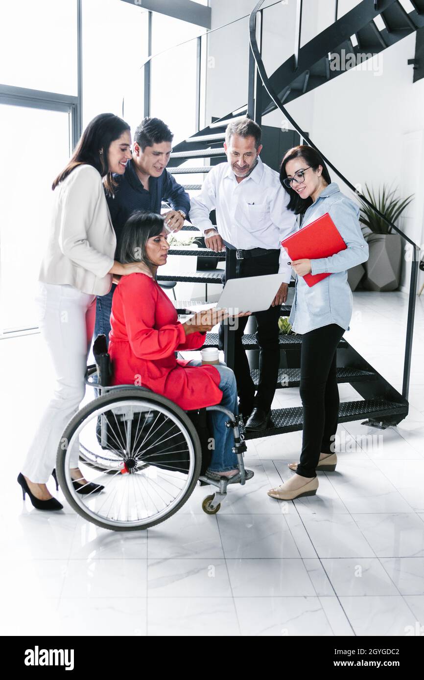 Group of latin business people standing on the staircase with transgender woman sitting on wheelchair in Latina America Stock Photo