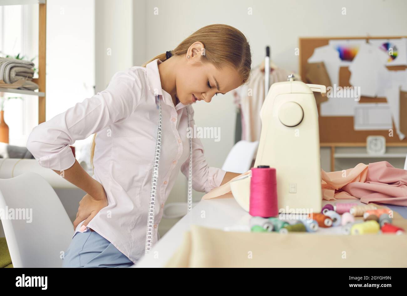 Tired woman who works as a tailor and has bad posture is suffering from back pain Stock Photo
